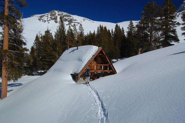 This is a photo showing a skier skiing towards Pear Lake Winter Hut, deeply covered in snow.<br />Photo by Douglas Leister